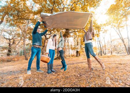 Sohn springt unter Picknickdecke, während die Eltern sich hinlegen parken Sie im Herbst Stockfoto