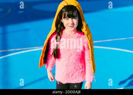 Nettes Mädchen trägt gepolsterte Jacke, während auf dem Sportplatz stehen Stockfoto