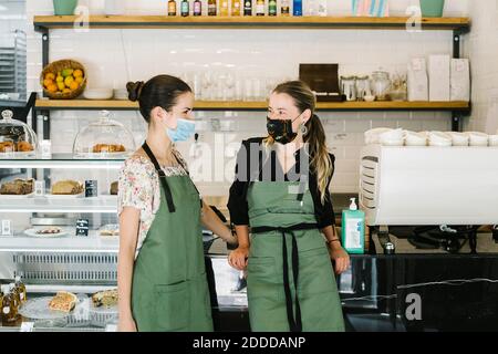 Geschäftsfrauen tragen Gesichtsmaske und Schürze an der Theke stehen Café-Bar Stockfoto