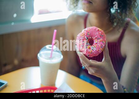 Junge Frau, die Donut isst, während sie im Café sitzt Stockfoto