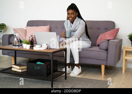 Junge Geschäftsfrau trinkt Kaffee während der Arbeit auf Laptop zu Hause Stockfoto
