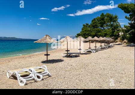 Leerer Strand mit Liegestühlen und Sonnenschirmen in Kroatisch Makarska. Kiesstrand ohne Menschen Stockfoto