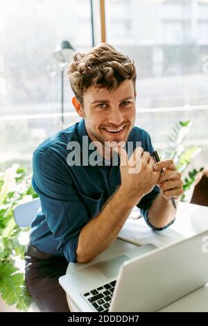 Lächelnder, hübscher junger Geschäftsmann, der mit einem Laptop am Tisch sitzt Café Stockfoto