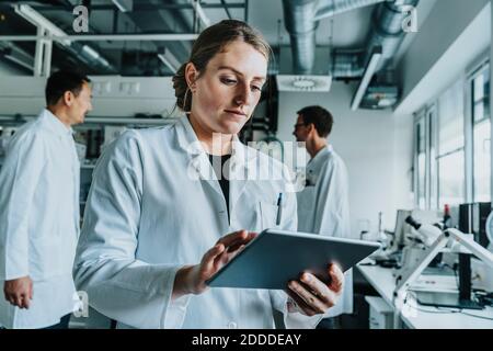 Junge Frau mit digitalem Tablet, während sie mit einem Kollegen im Stehen steht Hintergrund im Labor Stockfoto