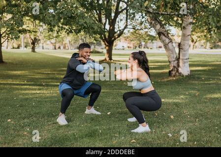 Lächelndes Paar, das zusammen hockende Übung macht, während es im Hinterhof steht Stockfoto
