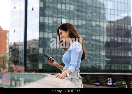 Lächelnde junge Geschäftsfrau, die Smartphone benutzt, während sie auf dem Steg steht Stockfoto