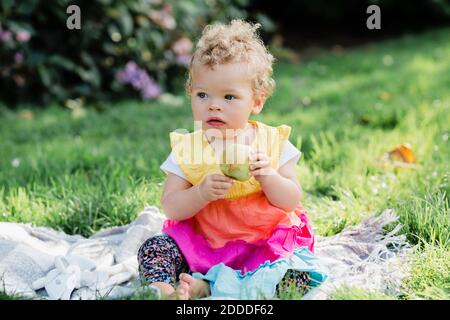 Nettes Baby Mädchen hält Obst, während auf Gras sitzen parken Stockfoto