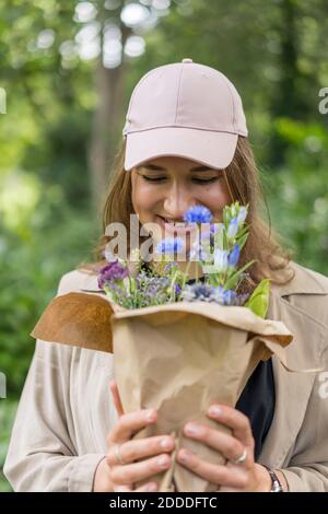 Schöne junge Frau lächelt, während Blick auf Blumenstrauß Im Park stehen Stockfoto