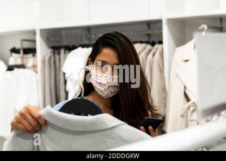 Frau trägt Schutzmaske beim Blick auf Kleidung im Einkaufen einkaufszentrum Stockfoto