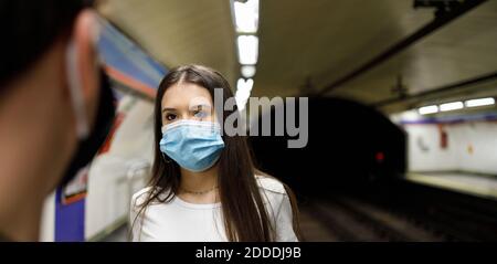 Junge Frau trägt Gesichtsmaske Blick auf den Mann während des Stehens An der U-Bahn-Station Stockfoto