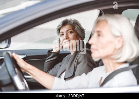 Geschäftsfrau lächelt, während sie bei einer Kollegin sitzt, die mit dem Auto fährt Stadt Stockfoto