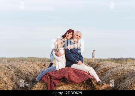 Enkelin mit Großeltern auf Heuballen gegen Himmel am Wochenende Stockfoto