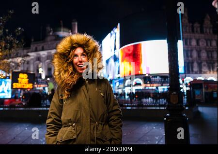 Lächelnde Frau in warmer Kleidung, die während der Weihnachtszeit in London, Großbritannien, auf der Regent Street steht Stockfoto