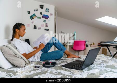 Teenager-Mädchen schreiben im Übungsbuch, während sie auf dem Bett sitzen Zu Hause Stockfoto