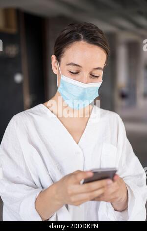 Geschäftsfrau trägt Gesichtsmaske mit Handy, während Sie stehen Büro Stockfoto
