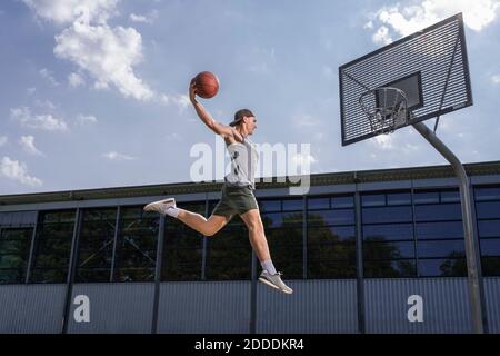 Junge männliche Athlet üben Dunking Ball in Basketball-Reifen auf Sonniger Tag Stockfoto