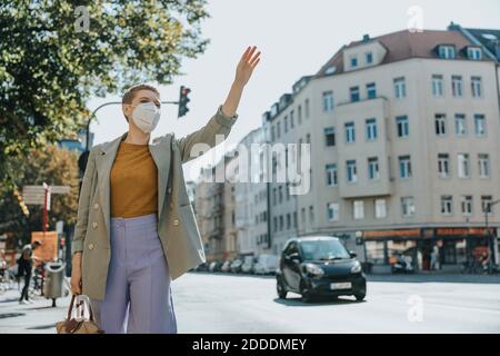 Frau trägt schützende Gesichtsmaske rufen Taxi durch winken stehen Auf der Straße in der Stadt Stockfoto