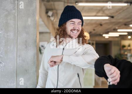 Lächelnder Hipster Mann tun Ellbogen Beule mit weiblichen Freund während Zu Hause stehen Stockfoto