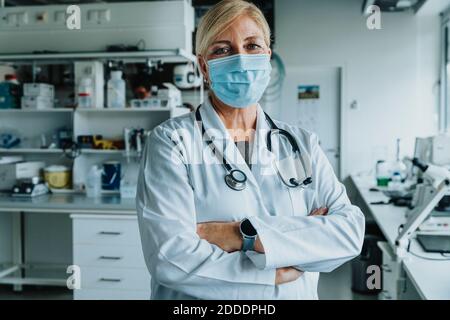 Selbstbewusste Wissenschaftler trägt Gesichtsmaske stehen mit Armen gekreuzt an Labor Stockfoto