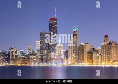 Beleuchtete Ansicht von 875 North Michigan Avenue (John Hancock Center) umgeben von Wolkenkratzern in der Abenddämmerung, Chicago, USA Stockfoto