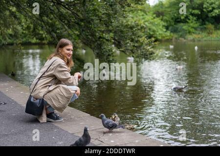 Junge Frau hockend auf Bürgersteig nahe See Stockfoto