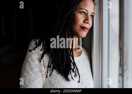 Betrachtende Frau, die durch das Fenster schaut, während sie zu Hause steht Stockfoto