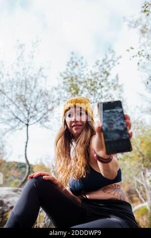 Frau mittleren Erwachsenen zeigt Handy, während sie im Wald in La Pedriza, Madrid, Spanien sitzt Stockfoto