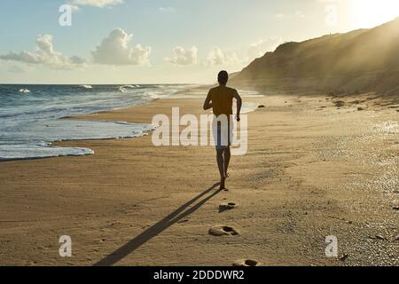 Mann joggt am Strand bei Sonnenuntergang Stockfoto
