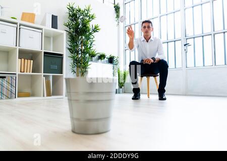 Gelangweilte männliche Unternehmer werfen zerknitterten Papierkugel in Mülleimer an Büro Stockfoto