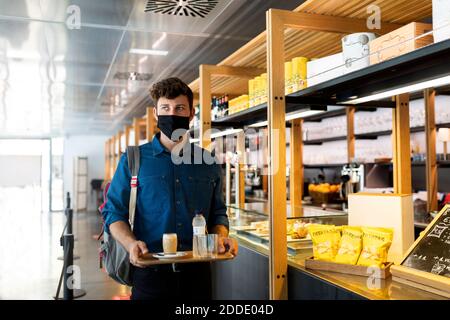 Geschäftsmann in Schutzmaske hält Tablett mit Getränken in Cafe während der COVID-19 Stockfoto