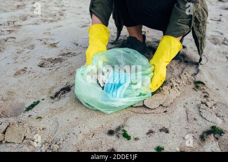 Frau sammelt Einweg-Gesichtsmaske in Müllbeutel während der Reinigung Strand Stockfoto