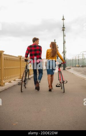 Lächelndes heterosexuelles Paar mit Fahrrad auf dem Bürgersteig in der Stadt Stockfoto