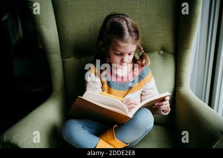 Nettes Mädchen schreiben im Buch, während auf Stuhl sitzen Zu Hause Stockfoto