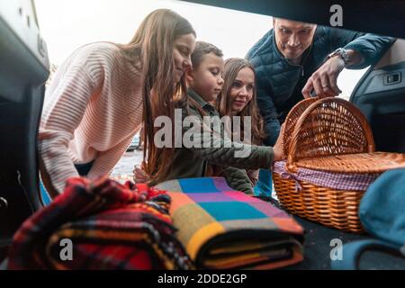 Lächelnde Familie, die Picknicksachen vom Kofferraum abholt Stockfoto
