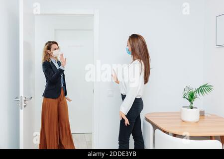 Frau trägt Gesichtsmaske winkende Hand an der Tür im Büro Stockfoto