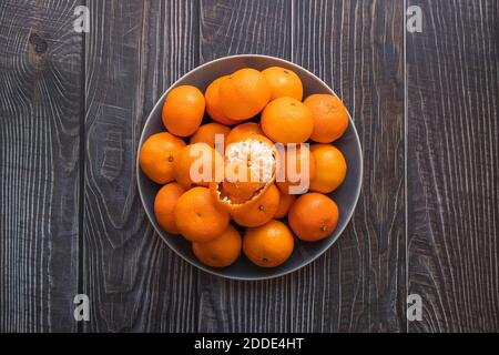 Eine Platte aus reifen orangen Mandarinen auf einem Holztisch, eine geschälte Mandarine auf der Oberseite Stockfoto