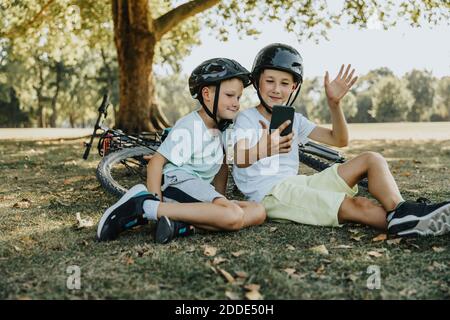 Brüder, die Videoanruf auf dem Smartphone machen, sitzen in der Öffentlichkeit parken Stockfoto