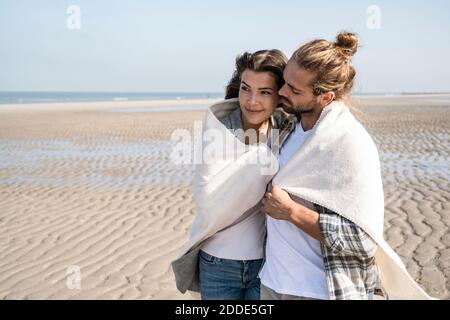 Romantisches junges Paar mit Decke am Strand stehend bedeckt Stockfoto