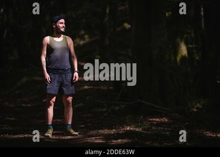 Lächelnder Mann in Sportkleidung, der wegschaut, während er ansteht Wald Stockfoto