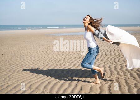 Sorglose junge Frau läuft, während sie Decke am Strand hält Sonniger Tag Stockfoto