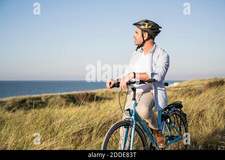 Mann, der auf die Ansicht schaut, während er auf dem Fahrrad durch Gras sitzt Feld gegen klaren Himmel Stockfoto