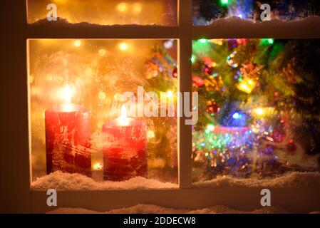 Nachtansicht von außerhalb eines Fensters für Weihnachten dekoriert.brennende Kerzen, entkochte Weihnachtsbaum und Lichter. Stockfoto