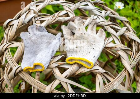 Ein Paar gebrauchte Arbeitshandschuhe, die auf einem Weidenkorb im Garten liegen, Nahaufnahme. Stockfoto