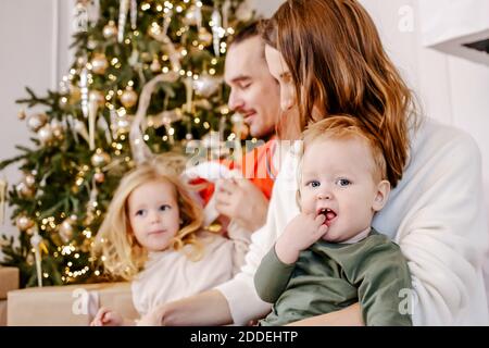 Portrait der freundlichen Familie sitzen zu Hause in der Nähe des Weihnachtsbaums, alle lächeln. Konzentrieren Sie sich auf das Baby. Stockfoto