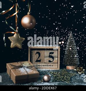 Holzblock Kalender mit 25 dezember Datum, Weihnachtsdekorationen und Geschenkbox auf schwarzem Hintergrund mit Funkeln. Stockfoto