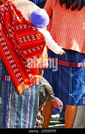 Eine Frau geht mit einem Baby durch den Chichi-Markt in Chichicastenango, Guatemala, und lebt die türkei im Schlepptau. Der farbenfrohe Zentralamerika-Markt ist einer der größten und ältesten in der Region und bringt Verkäufer, Händler, Käufer und Touristen in das Handelszentrum ein paar Stunden außerhalb der Hauptstadt Guatemala-Stadt, Guatemala. Stockfoto