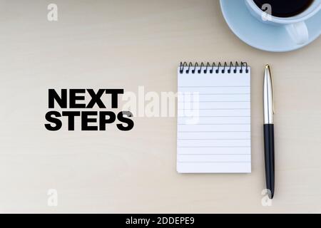 NÄCHSTE SCHRITTE Text mit Füllfederhalter und Tasse Kaffee auf Holzhintergrund.Business und Copy Space Konzept. Stockfoto