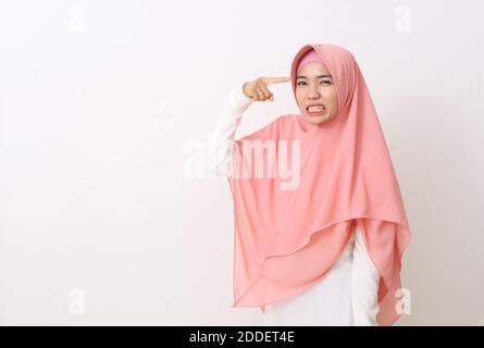 Ein Porträt asiatische muslimische Frau trägt einen rosa Schleier oder Hijab und weißes Kleid gestikulieren mit einem Finger gegen Tempel sagen, Sie sind verrückt. Zeigt auf h Stockfoto