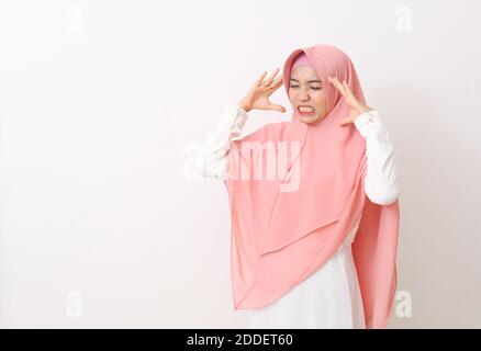 Ein Porträt einer asiatischen muslimischen Frau mit einem rosa Schleier oder Hijab und weißem Kleid bekam Kopfschmerzen. Sie berührte ihre Kopfbügeln mit beiden Händen und Leid Stockfoto