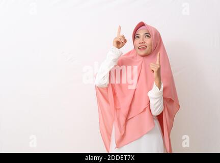 Ein Porträt einer glücklichen asiatischen muslimischen Frau, die einen Schleier oder Hijab trägt, der auf sie zeigt oder etwas über ihr präsentiert. Isoliert auf weißem Hintergrund mit Kopierrac Stockfoto